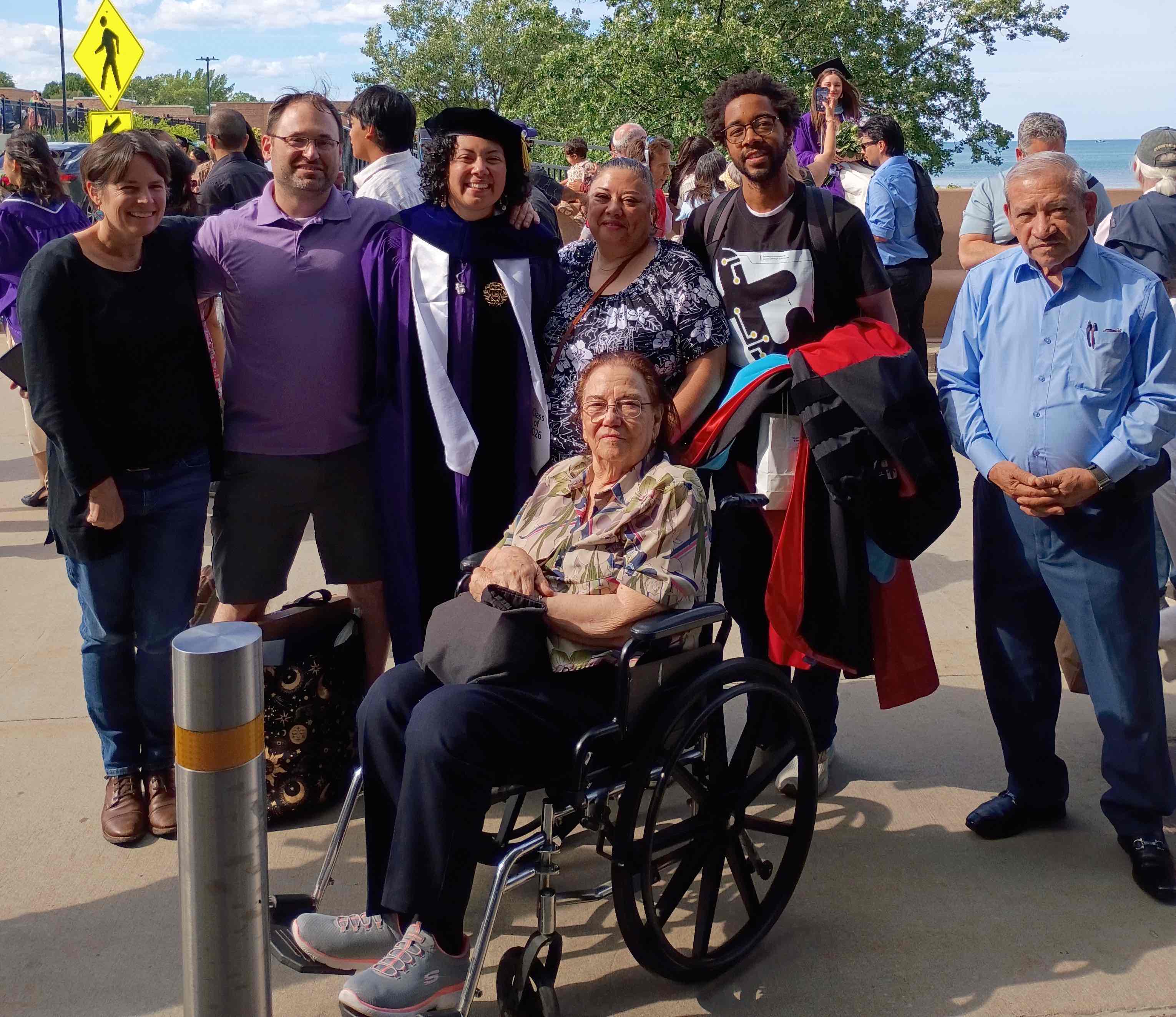 Outdoor group picture of V in their cap and gown, surrounded by loved ones.