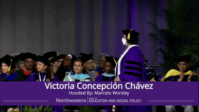an animated gif of V in their cap and gown wearing an N95 walking across the stage to be robed by their advisor
