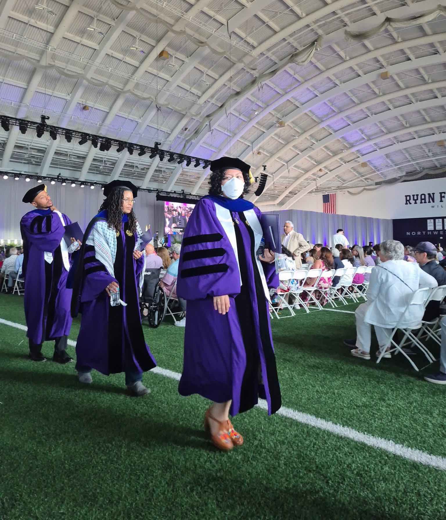 V in an Aura N95 mask walking in their cap and gown